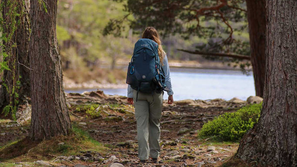 Person with a backpack walking through a forest towards a lake